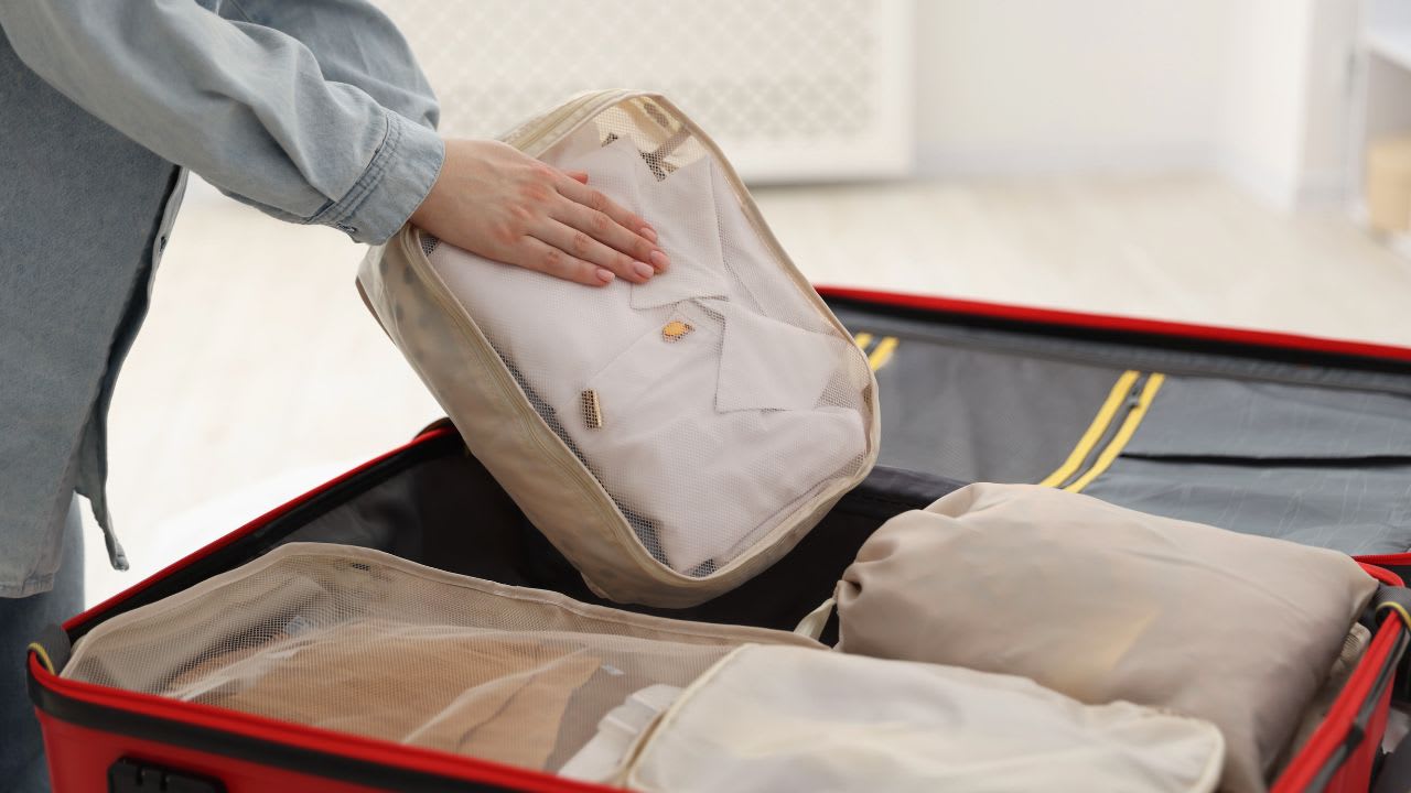 Woman Putting Packing Cube into Suitcase Indoors, Closeup. Pack for summer vacation